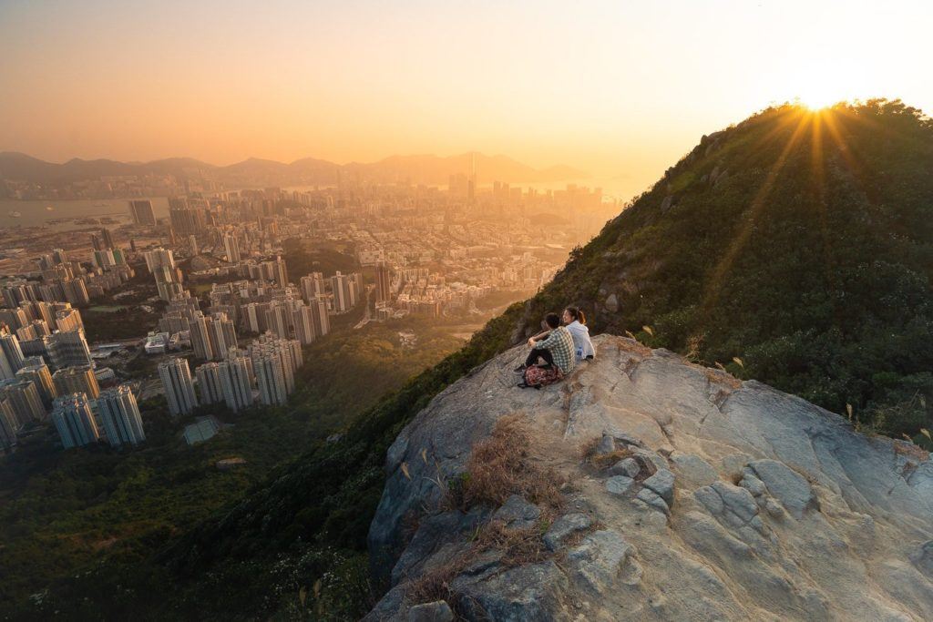Zwei Menschen sitzen auf einem Felsen und überblicken eine Stadt.