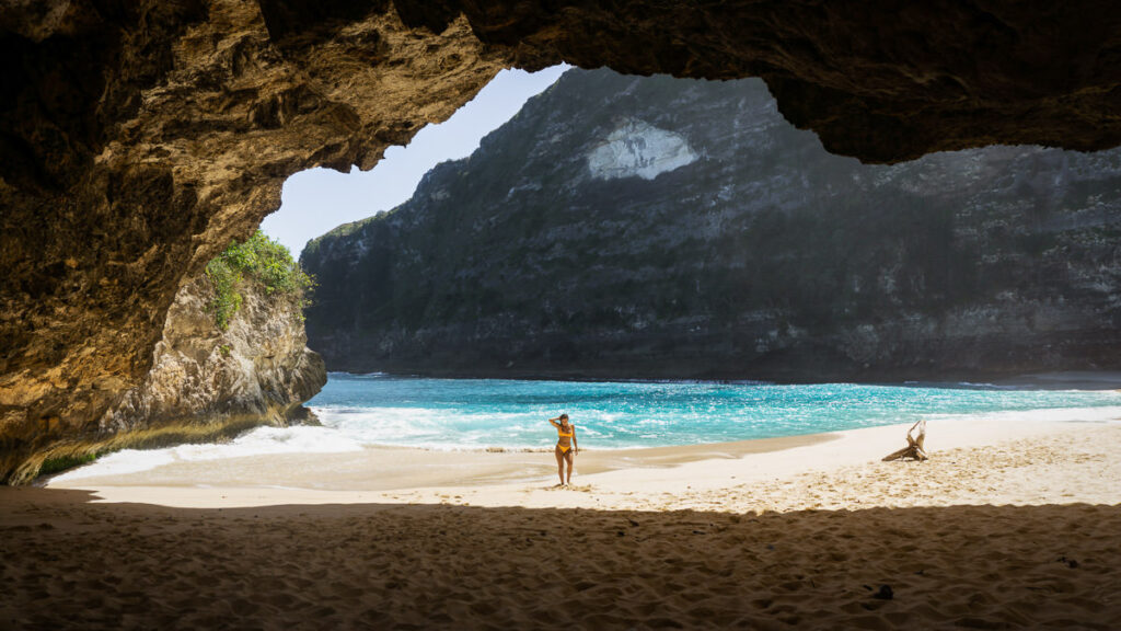 Eine Frau steht am Strand in der Nähe einer Höhle.