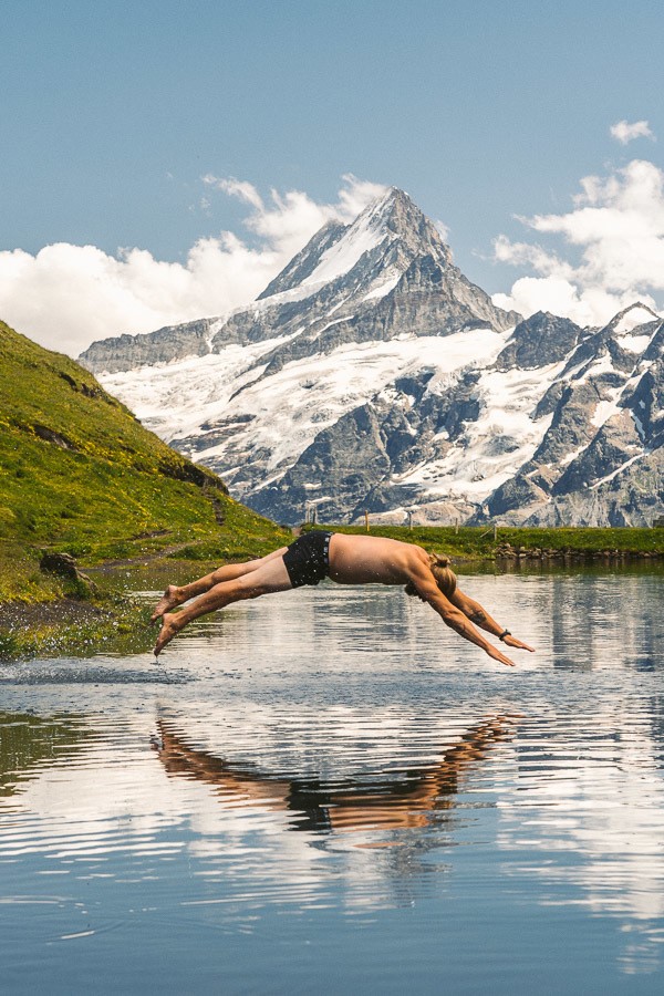 ein Mann taucht in einen See mit einem Berg im Hintergrund.