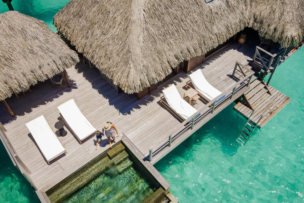 Ein Steg mit Stühlen und strohgedeckten Sonnenschirmen am Wasser in Französisch-Polynesien.