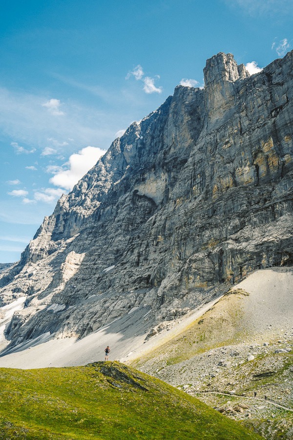 Eine Person, die einen grasbewachsenen Hügel hinaufgeht, mit einem Berg im Hintergrund.