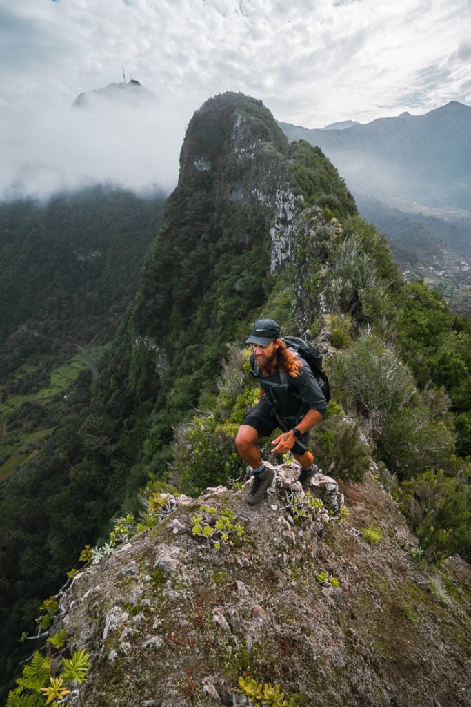 Ein Mann sitzt mit einem Rucksack auf einem Berggipfel.