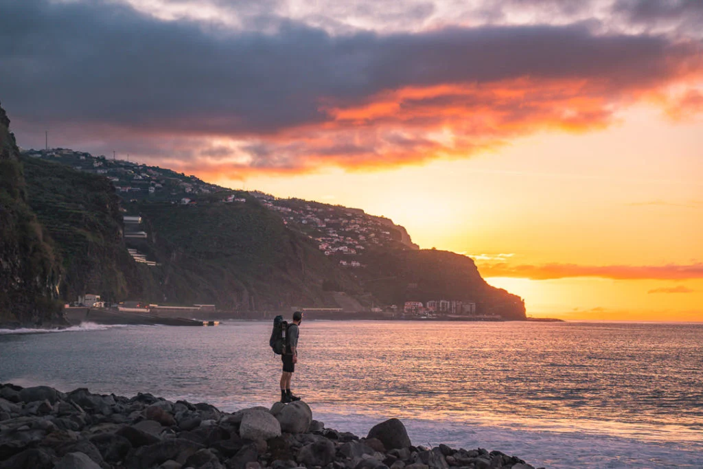 Eine Person, die bei Sonnenuntergang an einem felsigen Strand steht.