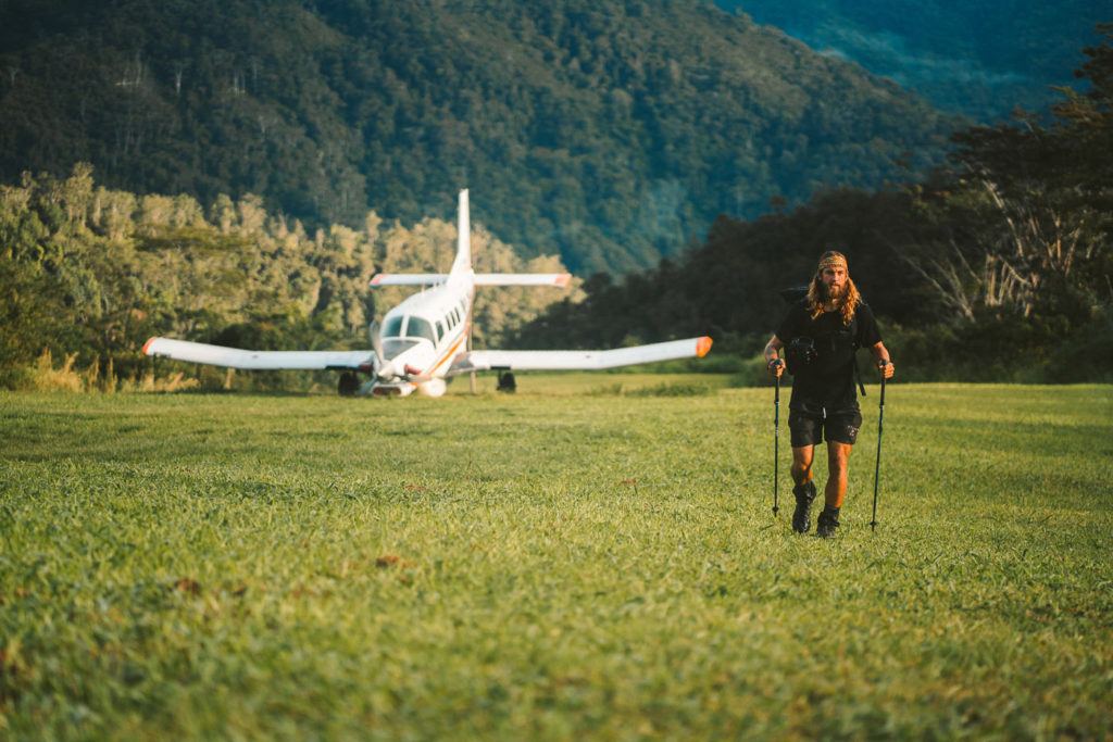 eine Frau, die neben einem kleinen Flugzeug über ein üppiges grünes Feld läuft.