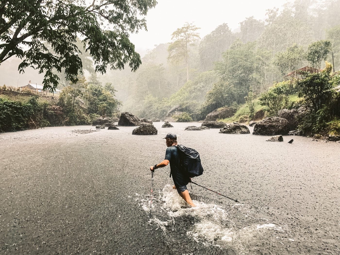 a man walking across a river in the rain.